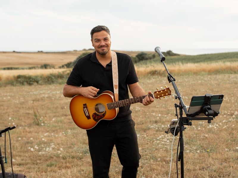 Kevin Hellot avec sa guitare et son micro en plein air, dans un paysage de la Côte d’Opale